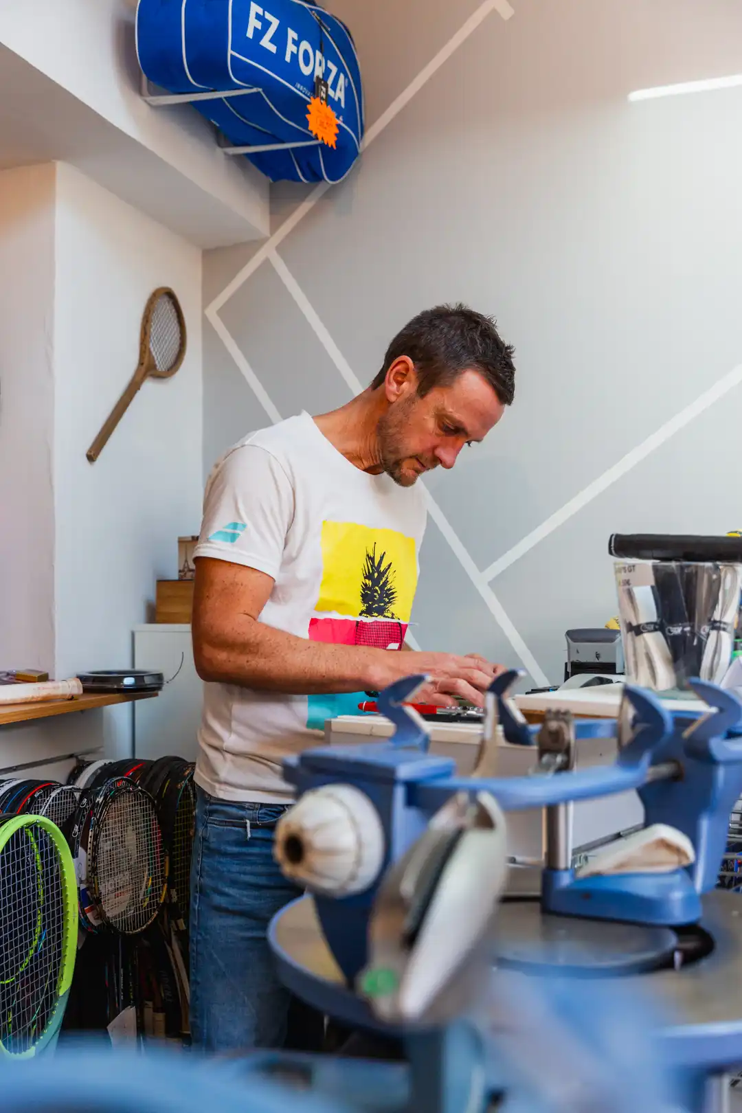 Gilbert ajuste avec précision la corde d'une raquette dans son atelier.
